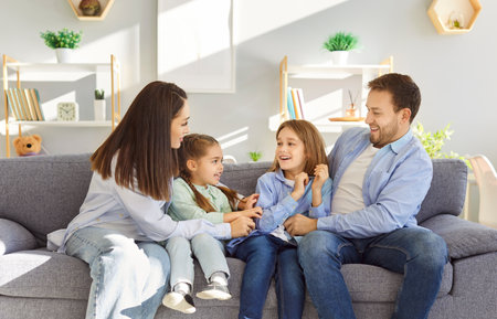 Happy smiling young family of four with two kids boy and girl sitting on sofa at home having fun and tickling resting on weekend. Portrait of parents with children. Family time and leisure concept.の写真素材