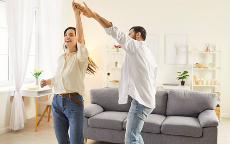Happy overjoyed smiling young couple having fun at home enjoying good mood and happy life moments together. Married man and woman dancing in the living room. Love, care and Valentines day concept.の写真素材