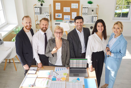 Group of business people men and women in formal clothes looking cheerful at camera indoors. Company employees standing at the desk on workplace in office. Teamwork and success concept.の写真素材