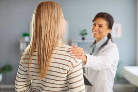 Joyful doctor informs her patient about positive changes in her health, gently touching shoulder. Doctor shows positivity and support to female patient who is standing with her back to camera.の写真素材