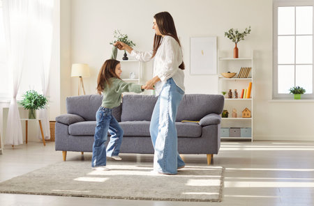 Happy joyful mother in casual clothes having fun and dancing with a child girl in the living room at home. Portrait of young female parent spending time together with daughter. Family time concept.の写真素材