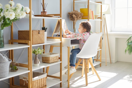 Little girl kid in modern playroom with accessories for game and study, enjoys creative hobby for children elementary development, interior of cozy nursing with whiteboard, comfortable furnitureの写真素材