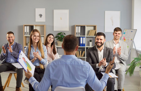 Group of smiling business professionals applauding speaker or leader during presentation in office. Cheerful corporate team showing appreciation while attending meeting or training session together.の写真素材