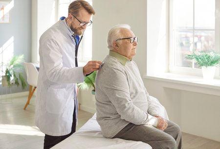 Professional doctor examining senior man patient, listening his breathing with stethoscope on back, providing medical checkup, giving medical care to senior people or older generationの写真素材