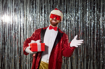 Portrait of happy man in Santa costume holding gift box during Christmas or new year party, filled with joy in a festive setting with warmth and celebration every moment of the evening.の写真素材