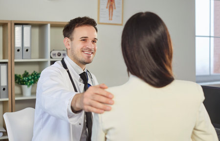 Portrait of smiling friendly male doctor therapist supporting his female patient in office. Physician sitting in medical clinic giving consultation a woman during examination. Medicine concept.の写真素材