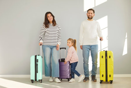 Mother, father with little cute child girl standing with luggage going to vacation holiday trip isolated on gray wall background Happy smiling family looking at camera ready for summer travel.の写真素材