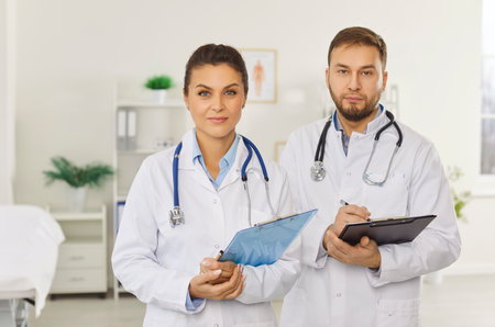 Portrait of a confident smiling young professional doctors in white uniform looking cheerful at camera standing in hospital or clinic. Medicine, medical staff and health care concept.の写真素材