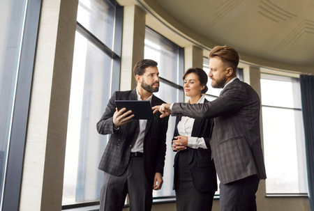 Real estate agent and business people watching tablet in modern office, talking to solve rent issues, realtor telling to clients to make recommendations and consulting on new property, advice givingの写真素材