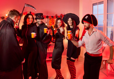 Happy young people group in carnival costumes dancing together celebrating Halloween party at home. Excited funny friends having fun on holiday in festive decorated living room. Celebration concept.の写真素材