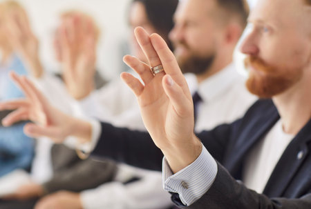 Close up of business person raising hand to ask or answer a question on a meeting. Group of people company employees in formal clothes voting sitting in a row during job conference in office.の写真素材