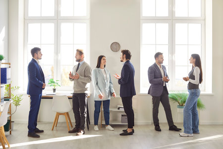 Group of young confident business people men and women talking in office during a meeting. Company employees working and discussing job and work projects indoors. Team work concept.の写真素材