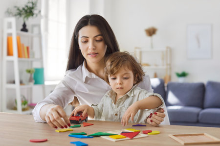 Portrait of child boy collecting wooden colorful geometric figures with mother sitting at table in living room at home. Young happy family playing in educational game with kid together.の写真素材