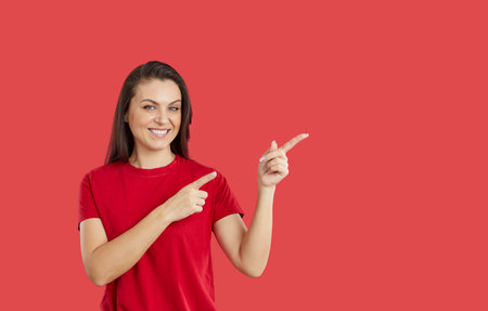 Portrait of smiling young woman isolated on red studio background point at empty blank copy space aside. Happy female recommend good sale offer or promotion deal. Client recommendation.の写真素材