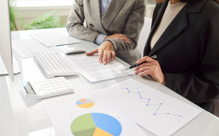 Close-up of business people in group working together on financial documents and chart in office, focusing on team collaboration in a professional setting with precision and analysis.の写真素材