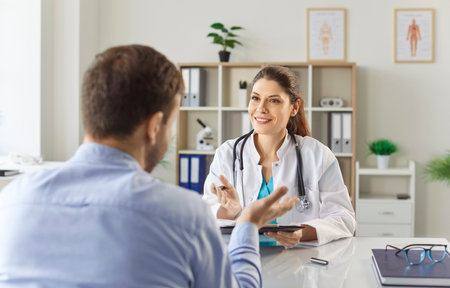Young man patient talking to female doctor in her office in clinic during medical examination. Woman physician listening to the patients complaints. Healthcare and medicine concept.の写真素材