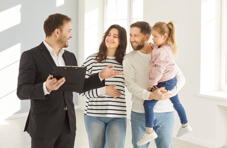Happy family talking to realtor as they look for house or apartment to rent or buy. Male agent, dressed in formal suit, holds clipboard and is explaining various options available for family.の写真素材