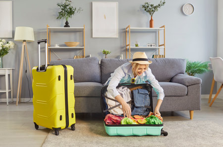 Satisfied woman packing suitcase at home, preparing for summer vacation or travel trip, organizing baggage for holiday in a cozy setting with excitement and anticipation for adventure.の写真素材