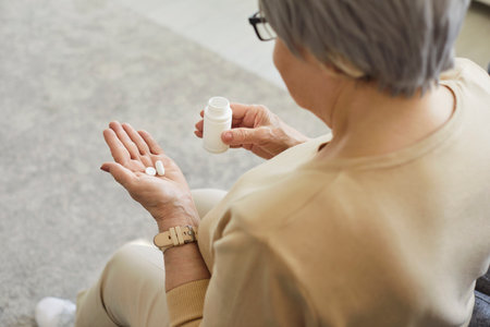 Back view of middle aged woman holding bottle of drugs, taking medicine prescribed by doctor, complex supplements, vitamins, taking care of her health, being at home, managing chronic painの写真素材