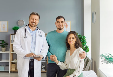 Portrait of smiling happy young couple husband and wife standing with a male family doctor therapist in medical clinic or hospital. Health care, family medicine and check up concept.の写真素材
