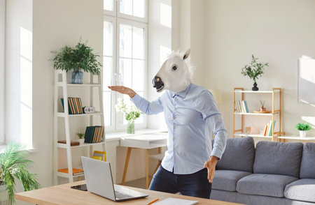 Funny extravagant happy man wearing horse head happy dance near laptop showing impressive achievements, successful deal, excessively wealth, cute amuse guy playingの写真素材