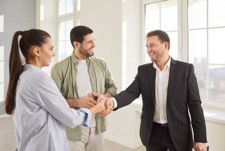 Realtor real estate agent hand shake deal with young family couple after showing, advertising new property to clients, helping to buy, rent home, consulting on market, price, mortgage, house for buyerの写真素材