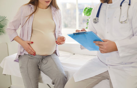 Doctor gynecologist meeting with pregnant woman patient in clinic, filling in medical form during checkup. Expecting mother coming on appointment, having consultation before giving birthの写真素材