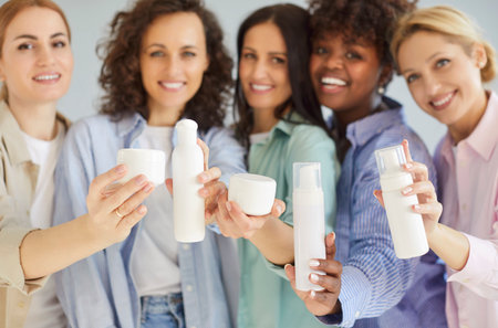 Multi ethnic friendly group of happy beautiful women showing bottle mockup for body treatment, spa procedures, beauty salon satisfied clients, attractive girls advertising female beauty care secretsの写真素材