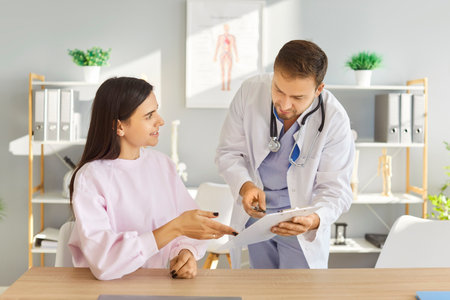 Young doctor man holding report file with appointment and prescribe treatment to a female cheerful patient sitting at the desk in clinic during medical examination. Medicine concept.の写真素材