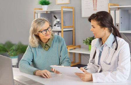 Caring nurse, doctor, physician explaining, talking to geriatric medicine caretaker with senior woman in clinic to help, support aged elder during medical visit, care, medical treatment for old peopleの写真素材