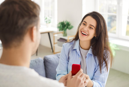 Man asking a romantic proposal to positive woman, presenting her with a gift ring. Their relationship blossoms with love, marking a memorable step toward marriage and a shared future.の写真素材