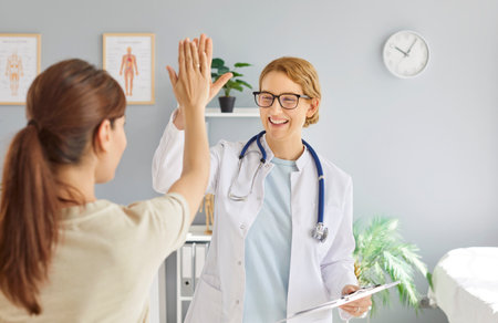 Friendly happy smiling female doctor rejoicing at success in treatment giving high five to woman patient standing in clinic after medical examination. Health care and medicine concept.の写真素材