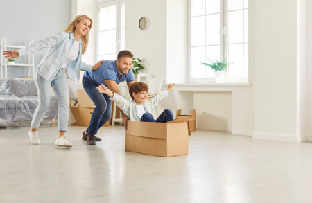 Happy family, new flat home owners, parents playing with cute small kid son on moving day, tenants, renters homeowners and child having fun riding in cardboard box in living room, relocatingの写真素材