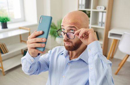 Funny young businessman using smart phone watching screen, smiling male professional holding smartphone working with business apps, texting sms, busy reading corporate message on mobile deviceの写真素材