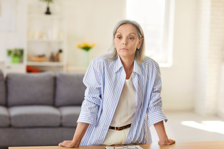 Portrait of a serious elderly woman standing in home office, focused and contemplative. Pensioner or grandma professional demeanor, showcasing a concentrated and thoughtful expression.の写真素材
