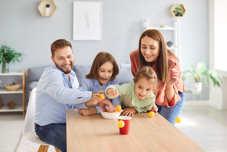 Happy parents having fun with their children during leisure time. Cheerful laughing family mother, father, daughter and son throwing balls into paper cup, having competition on weekend.の写真素材