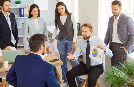 Group of cheerful business people sitting at desk on workplace discussing job and work projects in office on meeting. Company employees listen to their male colleague with a report during conference.の写真素材