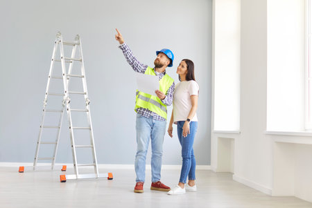Smiling young woman homeowner standing with foreman in new empty apartment and discussing a design project or repair. Meeting with builder about interior decoration. Moving concept.の写真素材