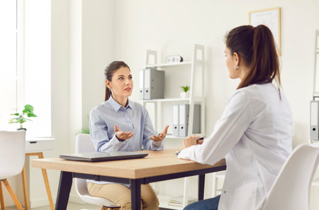 Patient having a medical consultation and conversation with a doctor or nurse in a hospital office. Healthcare professional providing advice and the patient seeking guidance regarding health.の写真素材