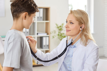 Female doctor listening to boys lungs with stethoscope, close-up. Pediatrician in clinic checking teenagers health. Concept doctor examining lungs, pneumonia, cold, coughの写真素材