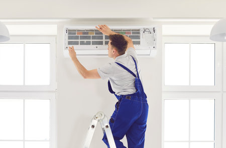Worker or electrician is inspecting an air conditioner system at home, conducting repair or maintenance work using a specialized instrument. The focus is on home HVAC system service.の写真素材