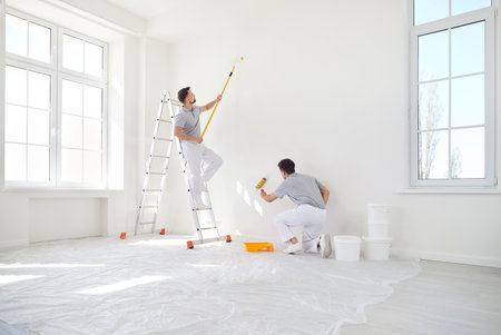 Team of male professional painters is working together to paint a wall during a renovation project at a home or office. Teamwork and dedication to improving the space in the construction area.の写真素材