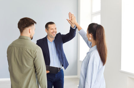 Young couple gives a high five to a realtor or real estate agent, confirming the purchase or rental of a property. Agreement during the apartment buying process in a professional setting.の写真素材