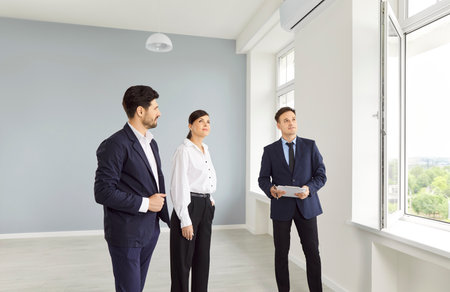 Real estate agent shows people an empty house. Business concept for office sales, commercial offer. Meeting of the architect with the clients of the project, consultation with the designerの写真素材