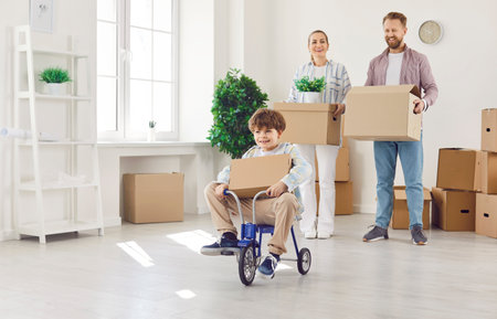 Son celebrating the relocation to a new home or estate with parents, joyfully riding tricycle. Excitement and happiness of the family moving, as they embark on a new chapter together.の写真素材