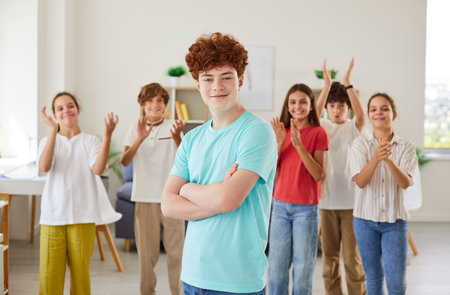 Portrait of a happy redhead schoolboy stands in front of classmates in the classroom. Joy of education and learning, highlighting the student enthusiasm for back to school experiences.の写真素材