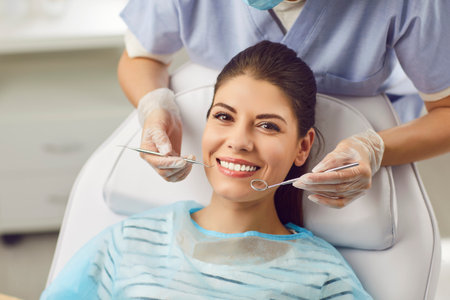 Beautiful young woman smiling while sitting at the dentist, close-up. Dentist holding instruments. Dental treatment in the clinic. Professional orthodontist medical care, medical equipment.の写真素材