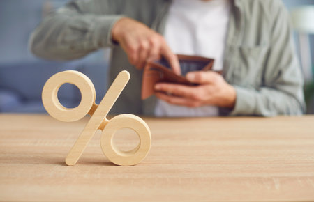 Wooden sign of present on table with a man sitting at the desk in casual clothes and holding open empty wallet in his hands in background. The concept of financial debts, loan and bankrupt conceptの写真素材