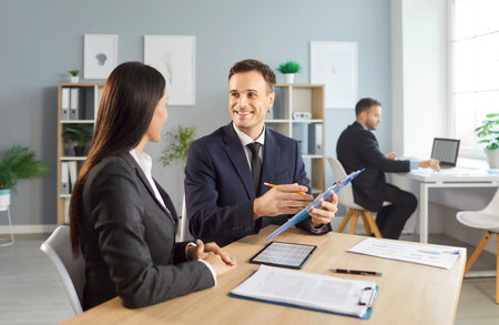 Happy business colleagues, accountants, engaged in conversation in the office. Teamwork reflects active collaboration and a finance focused meeting, emphasizing working together professionally.の写真素材