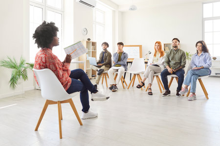 Businesswoman conducts a presentation or meeting for her team of colleagues in an office setting. The group of people discusses business strategies and collaborates on work related projects.の写真素材